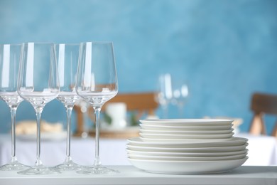 Stacked clean dishes and glasses on white shelf indoors