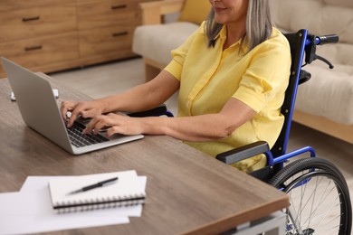 Photo of Woman in wheelchair using laptop at table indoors, closeup