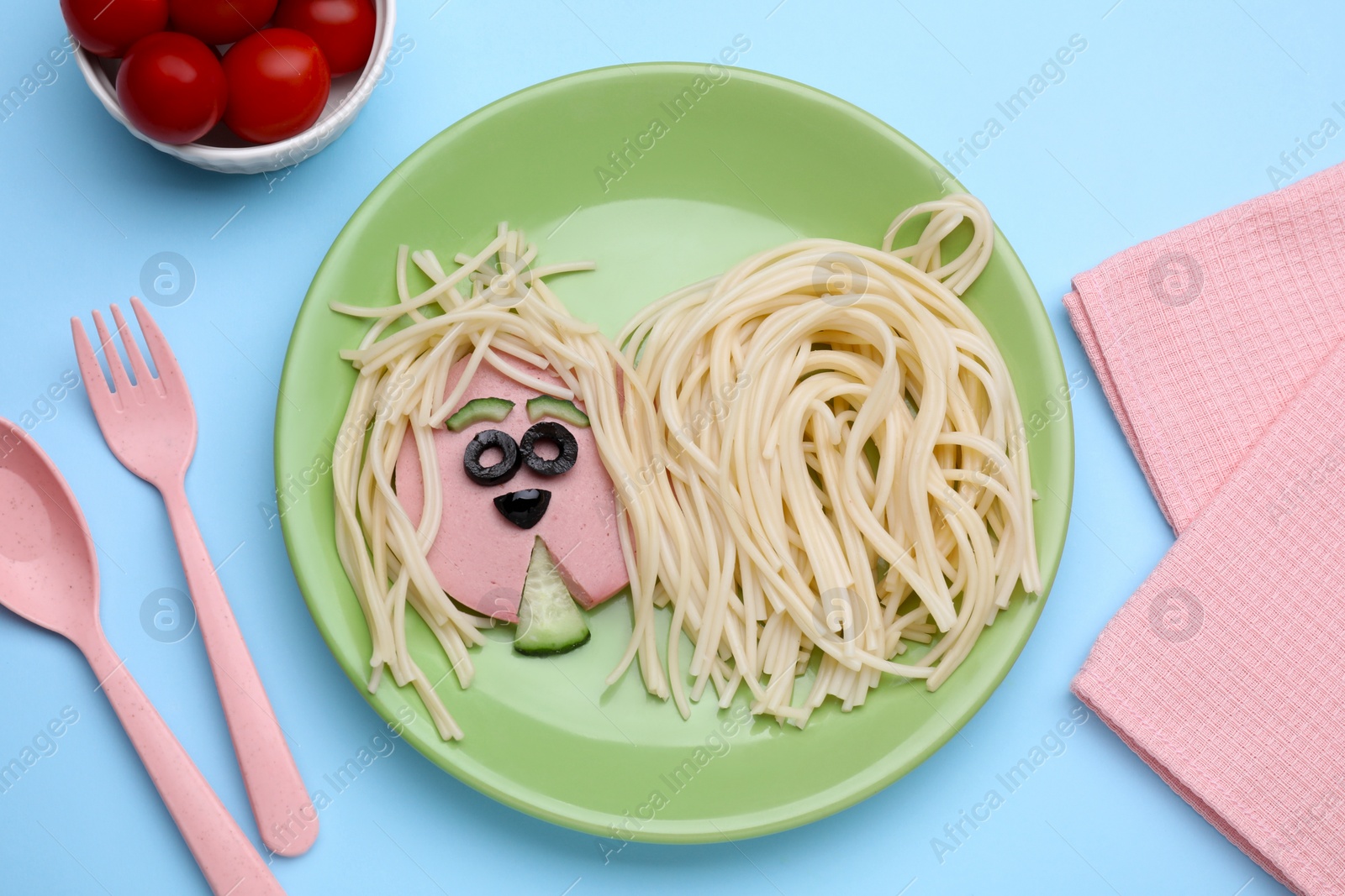 Photo of Creative serving for kids. Plate with cute dog made of tasty pasta, sausage and cucumber on light blue table, flat lay