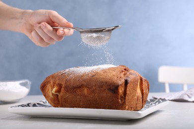 Photo of Woman sifting sugar powder onto fresh cake on light table, closeup
