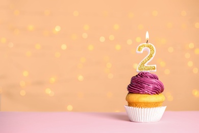 Photo of Birthday cupcake with number two candle on table against festive lights, space for text