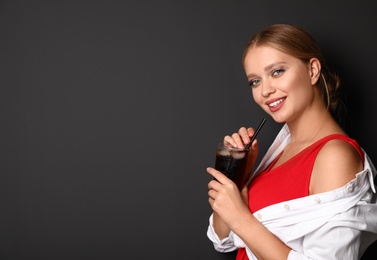 Photo of Young woman with glass of cola on black background, space for text. Refreshing drink