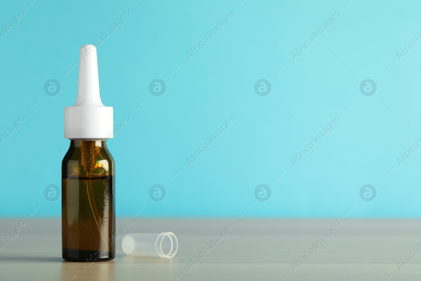 Photo of Bottle of nasal spray on table against light blue background, space for text