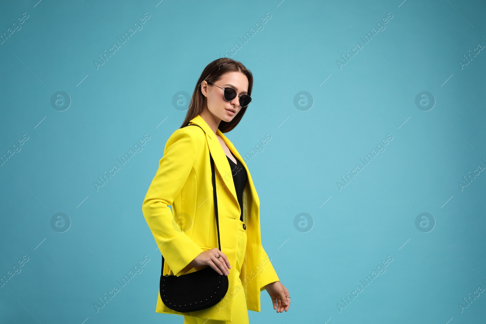 Photo of Fashionable young woman with stylish bag on light blue background