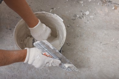 Worker plastering wall with putty knife indoors, closeup