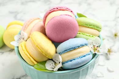 Delicious colorful macarons and flowers in bowl on white table, closeup