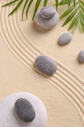 Photo of Zen garden stones and green leaves on sand with pattern, flat lay