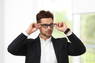 Portrait of handsome young man in elegant suit with glasses indoors