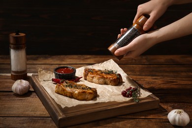 Food stylist grinding pepper onto meat medallions at wooden table in photo studio, closeup