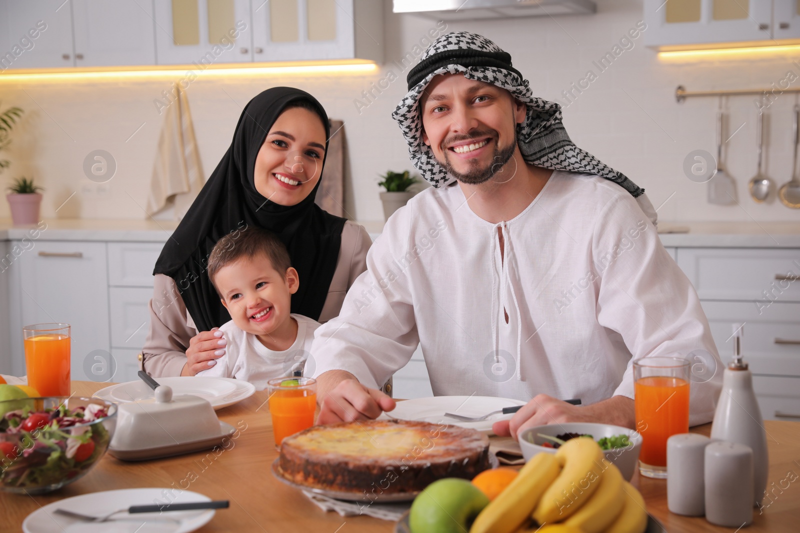 Photo of Happy Muslim family eating together at table in kitchen