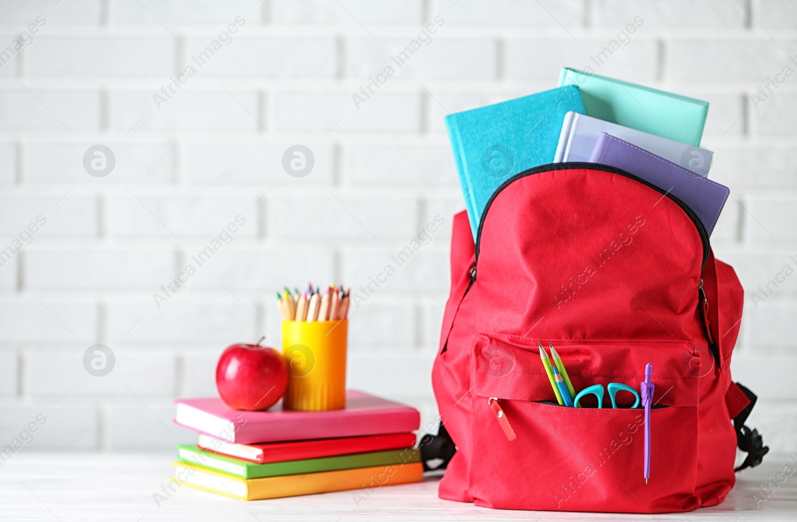 Photo of Backpack with school stationery on table against brick wall