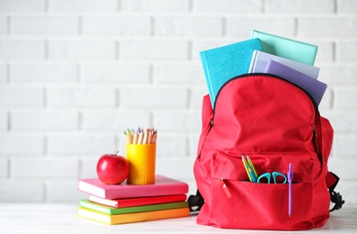 Photo of Backpack with school stationery on table against brick wall