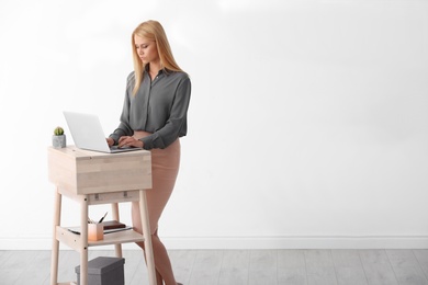 Photo of Young woman using laptop at stand up workplace against white wall. Space for text