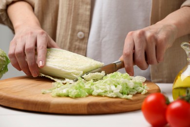 Photo of Woman cutting fresh chinese cabbage at white table, closeup