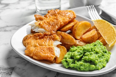 Photo of Plate with British traditional fish and potato chips on marble table, closeup