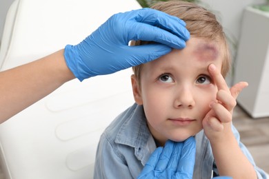 Doctor checking boy's forehead with bruise at hospital, closeup
