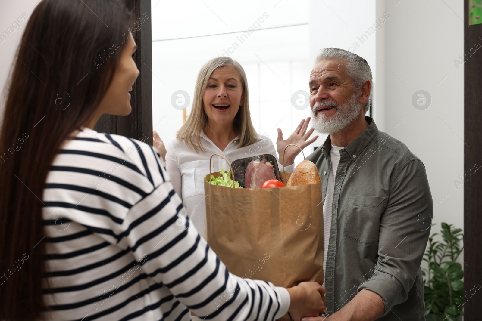 Photo of Courier giving paper bag with food products to senior couple indoors