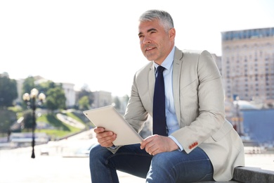 Photo of Portrait of handsome businessman with tablet in city, space for text