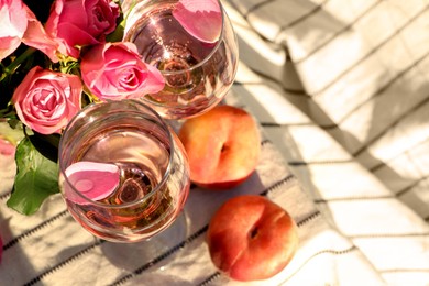 Glasses of delicious rose wine with petals, flowers and peaches on white picnic blanket outside, above view. Space for text