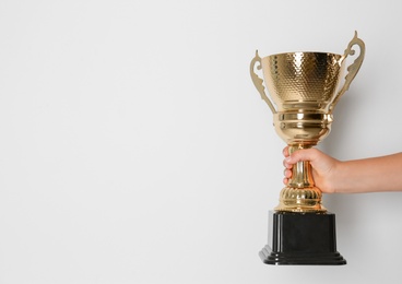 Child holding golden winning cup on light background, closeup. Space for text