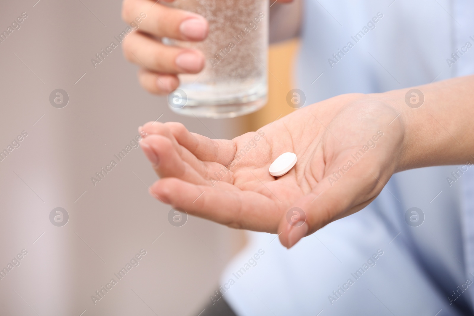Photo of Woman holding pill and glass of water on blurred background, closeup. Space for text