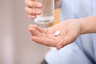 Woman holding pill and glass of water on blurred background, closeup. Space for text