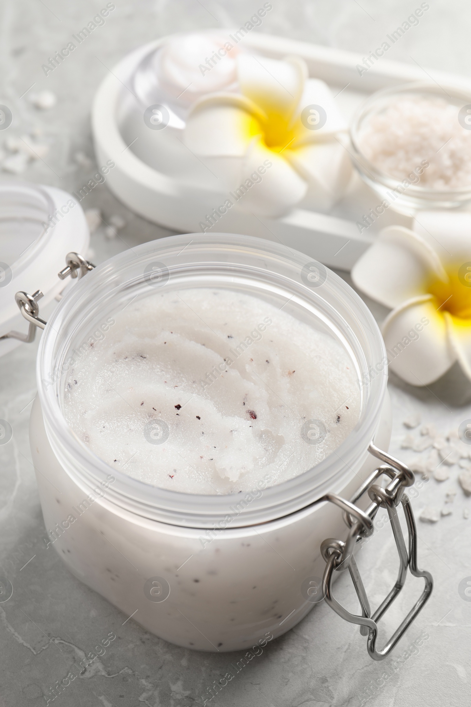 Photo of Body scrub in glass jar and plumeria flowers on grey marble table