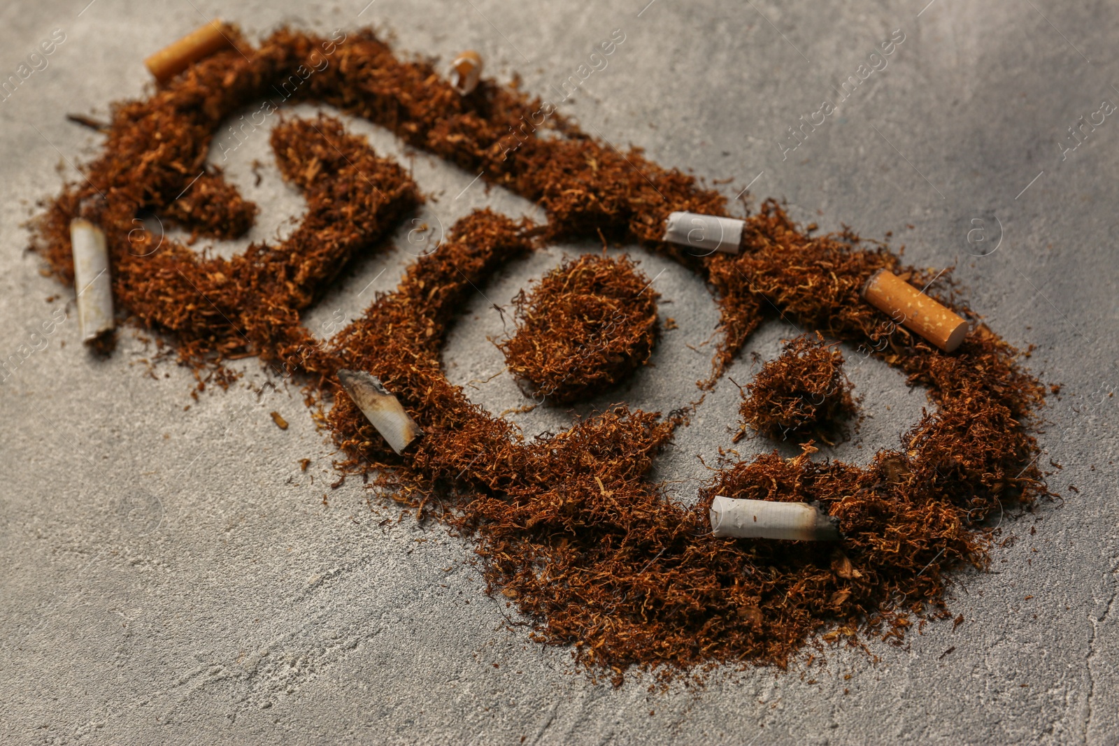 Photo of Word Stop made of tobacco and burnt cigarettes on grey textured table, closeup. No smoking concept