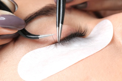 Photo of Young woman undergoing eyelashes extensions procedure, closeup