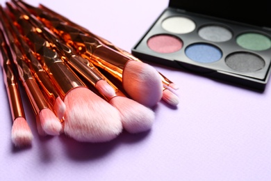 Photo of Professional makeup brushes and eye shadow palette on lilac background. Space for text