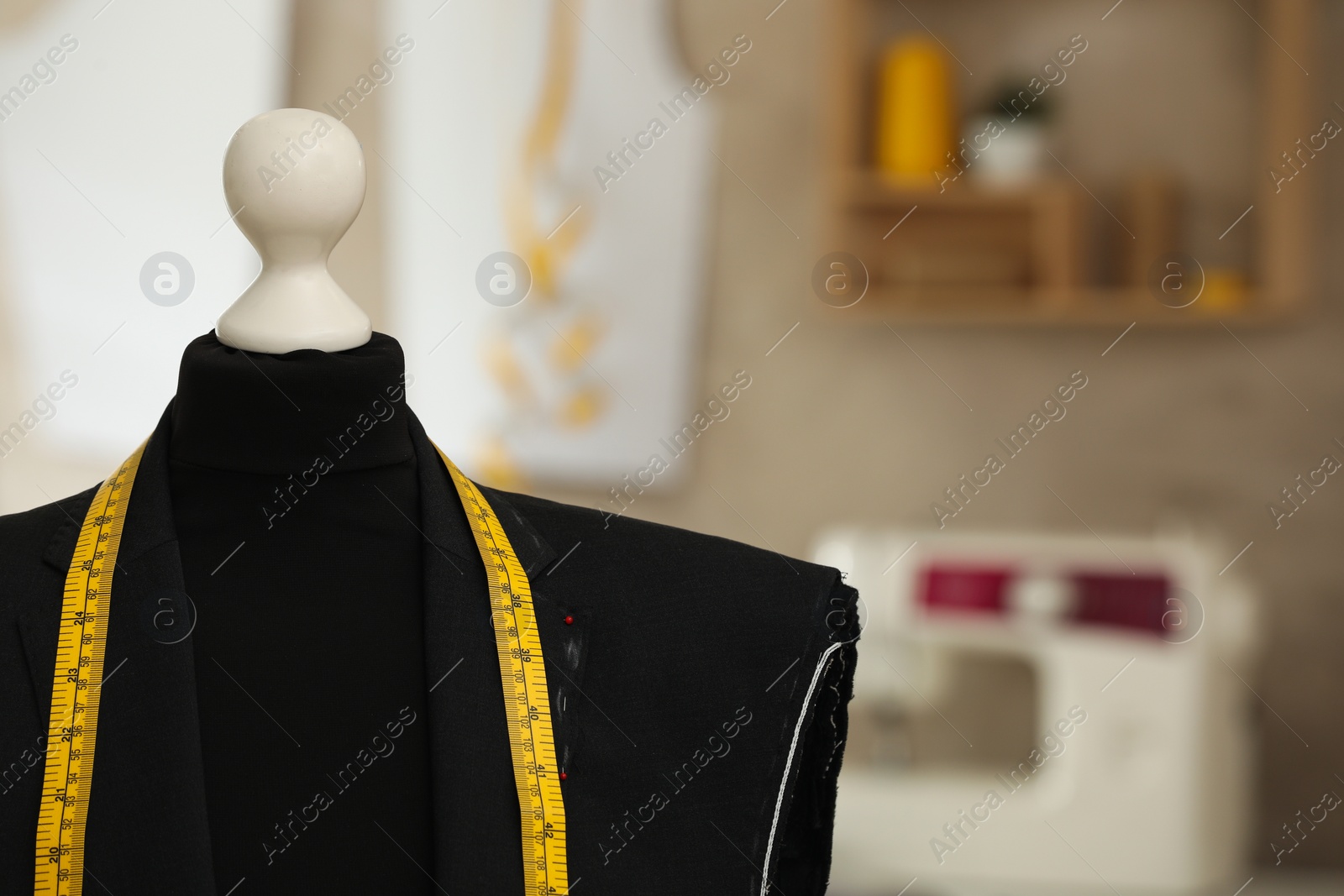 Photo of Mannequin with unfinished suit jacket and measuring tape in tailor shop, closeup. Space for text