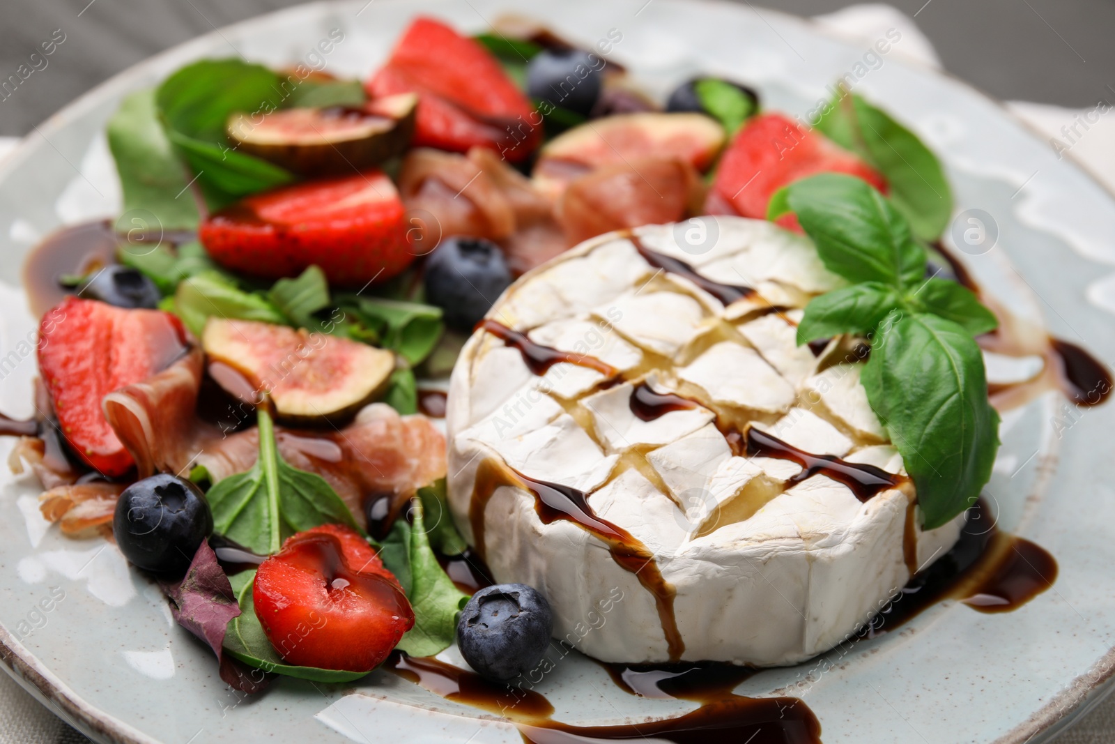 Photo of Delicious salad with brie cheese, berries and balsamic vinegar on plate, closeup