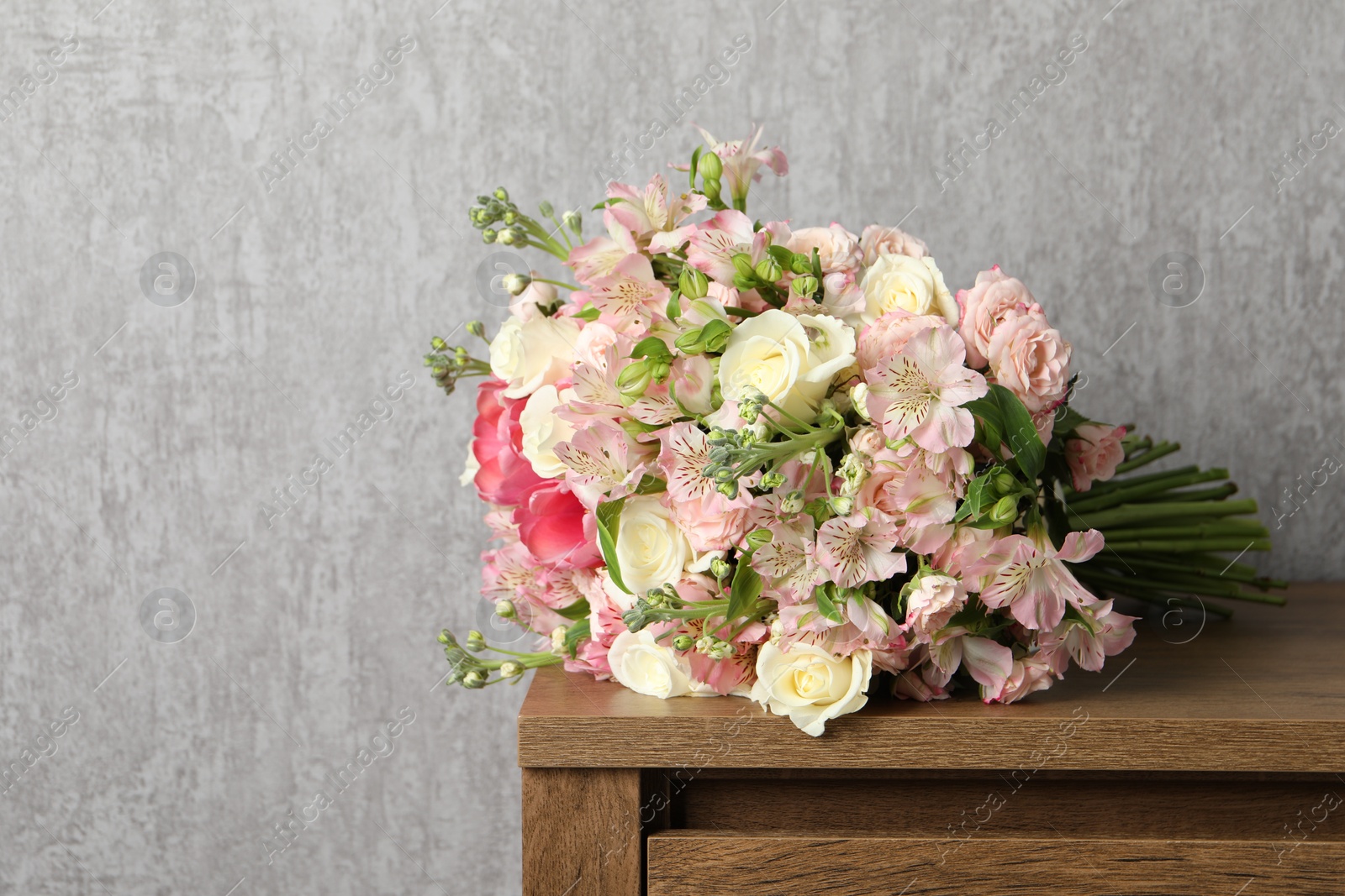 Photo of Beautiful bouquet of fresh flowers on wooden table near grey wall, space for text