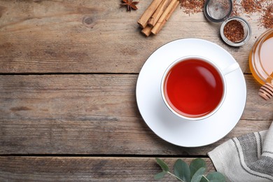 Freshly brewed rooibos tea, scattered dry leaves, honey and spices on wooden table, flat lay. Space for text