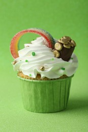 Photo of St. Patrick's day party. Tasty cupcake with sour rainbow belt and pot of gold toppers on green background, closeup