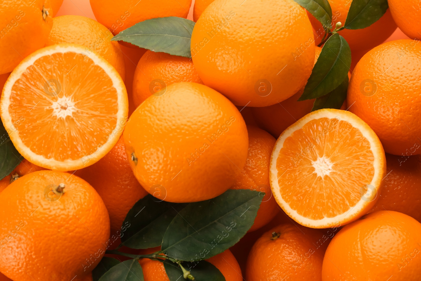 Photo of Cut and whole fresh ripe oranges with green leaves as background, top view