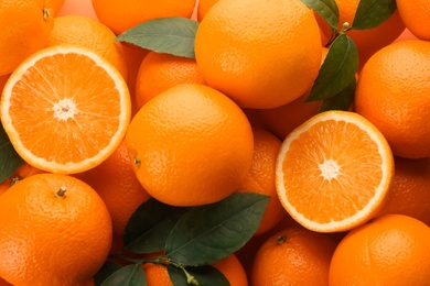 Cut and whole fresh ripe oranges with green leaves as background, top view