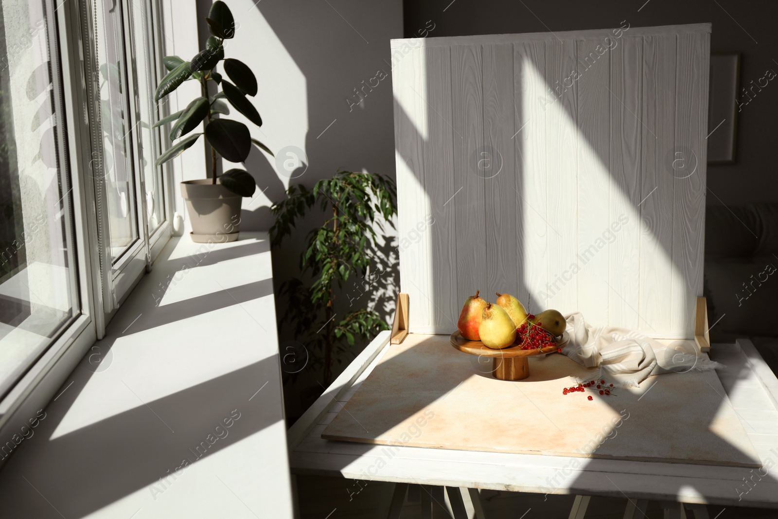 Photo of Stand with juicy pears, red currants and double-sided backdrop on table in photo studio