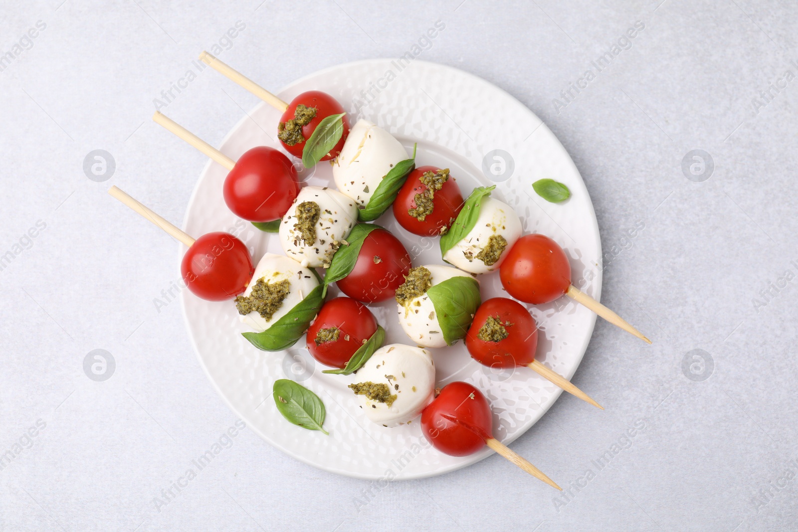 Photo of Caprese skewers with tomatoes, mozzarella balls, basil and pesto sauce on white table, top view