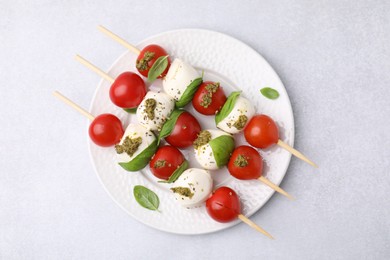 Caprese skewers with tomatoes, mozzarella balls, basil and pesto sauce on white table, top view