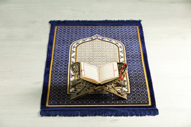 Photo of Rehal with open Quran and Misbaha on Muslim prayer rug indoors