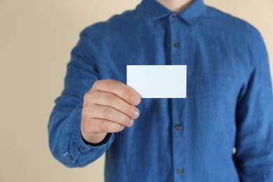 Man holding white business card on beige background, closeup