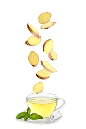 Image of Fresh sliced ginger falling into glass cup of tea on white background