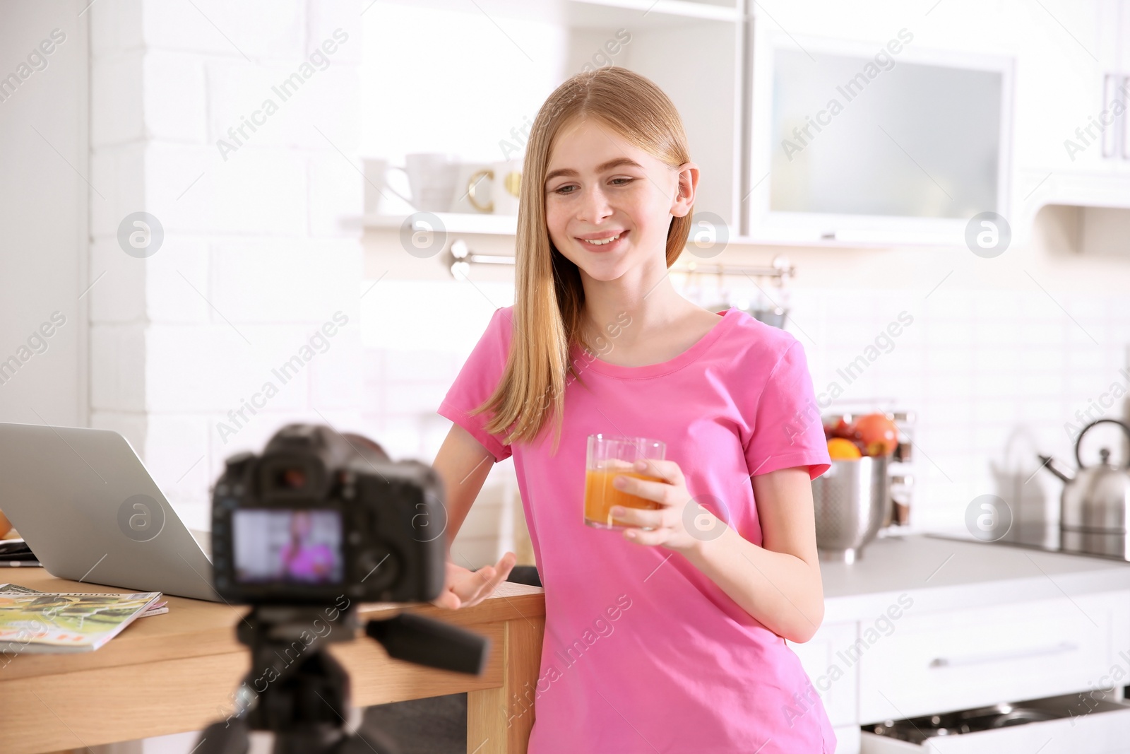 Photo of Cute teenage blogger with glass of juice recording video at table