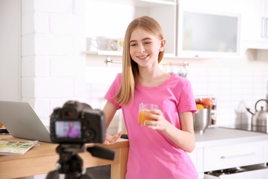 Cute teenage blogger with glass of juice recording video at table