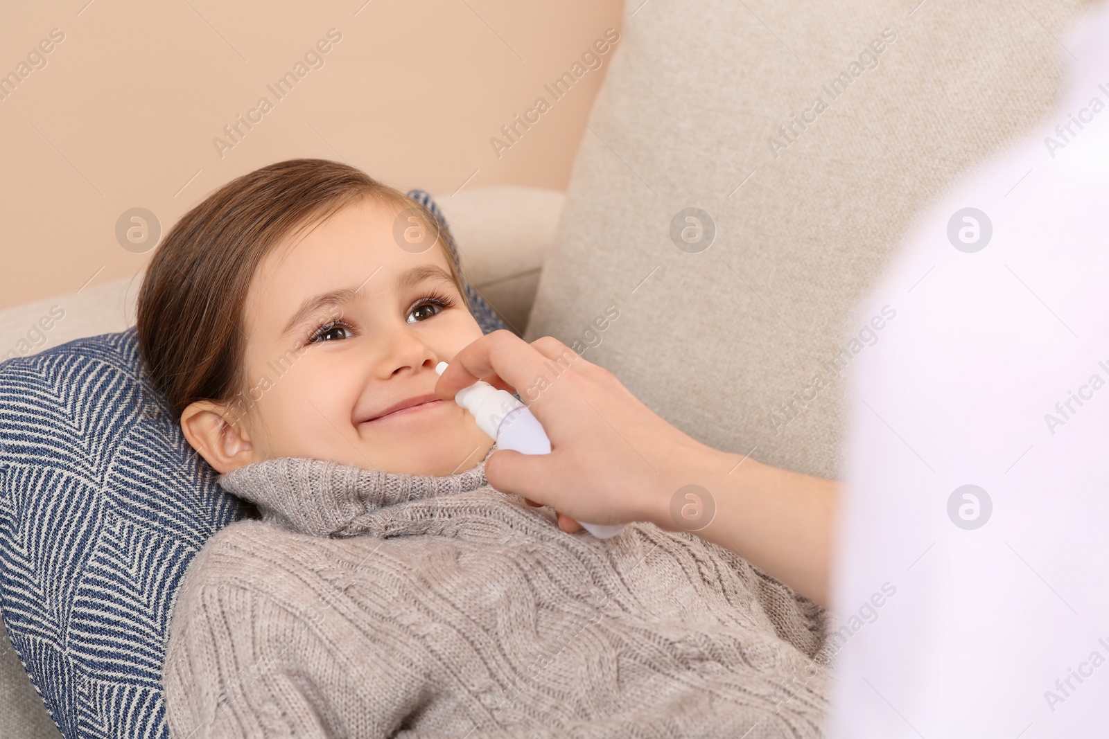 Photo of Mother using nasal spray to treat her little daughter on sofa, closeup