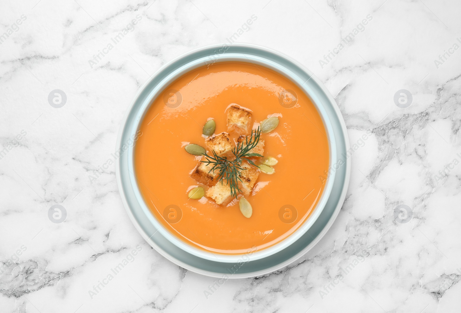 Photo of Tasty creamy pumpkin soup with croutons, seeds and dill in bowl on white marble table, top view