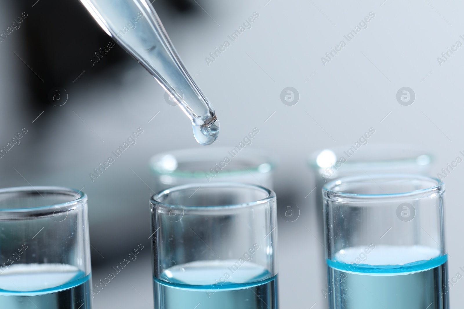 Photo of Dripping liquid from pipette into test tube on blurred background, closeup