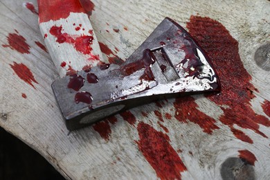 Axe with blood on wooden surface, closeup