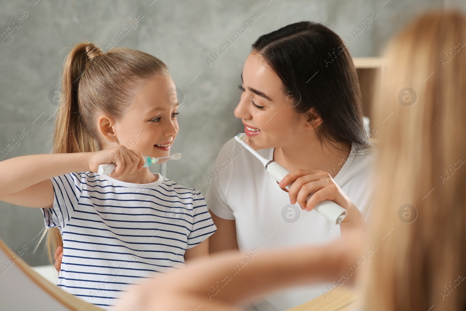 Photo of Mother and her daughter brushing teeth together near mirror in bathroom